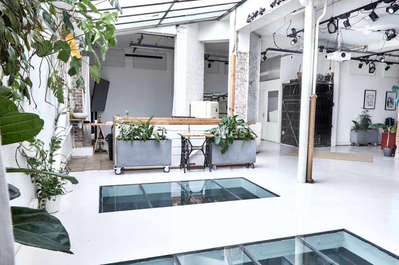 Espace lumineux avec verrière, sol blanc, plantes et dalles en verre laissant apparaître un niveau inférieur.