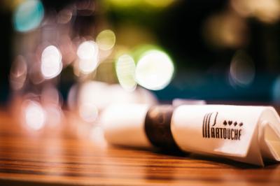Terrasse en bois avec table haute en rotin, fleurs blanches et vue sur une salle de restaurant moderne éclairée.
