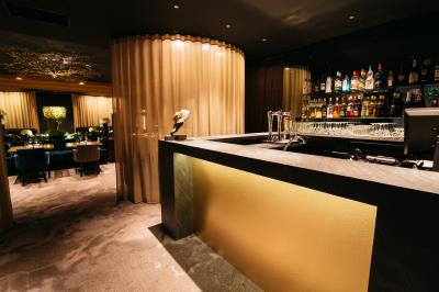 Terrasse en bois avec table haute en rotin, fleurs blanches et vue sur une salle de restaurant moderne éclairée.