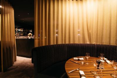 Terrasse en bois avec table haute en rotin, fleurs blanches et vue sur une salle de restaurant moderne éclairée.