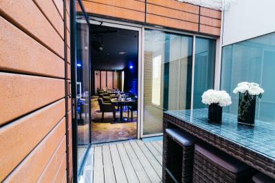 Terrasse en bois avec table haute en rotin, fleurs blanches et vue sur une salle de restaurant moderne éclairée.