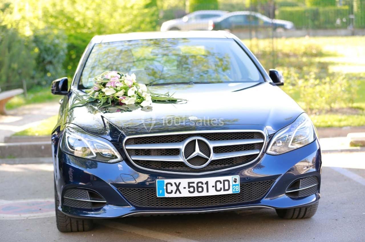 Voiture noire décorée de fleurs sur le capot, stationnée en extérieur par une journée ensoleillée.