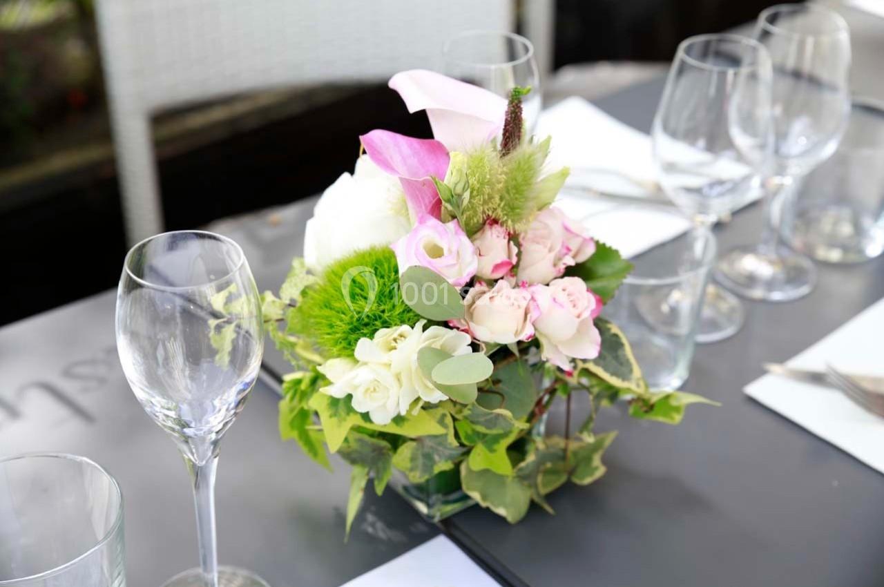 Centre de table floral avec roses, feuillage vert et verres à vin disposés sur une table grise.