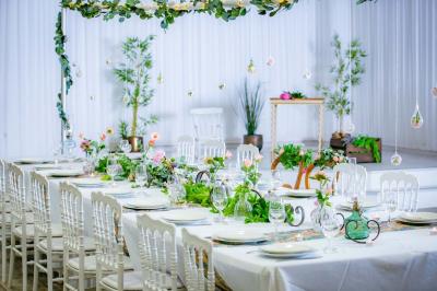 Table ronde avec verres vides, assiettes empilées, couverts, serviettes et desserts en arrière-plan.