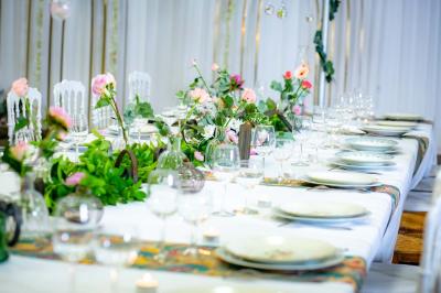 Table ronde avec verres vides, assiettes empilées, couverts, serviettes et desserts en arrière-plan.