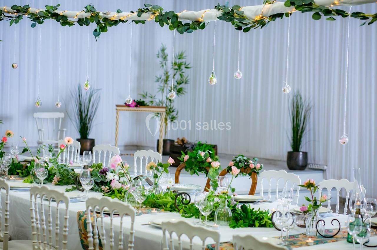 Salle de réception décorée avec des guirlandes lumineuses, des tables ornées de fleurs et une ambiance élégante.