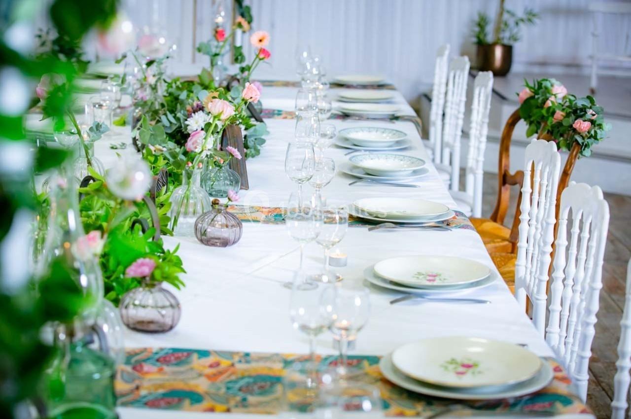 Table décorée avec des assiettes, verres et fleurs, disposée pour un repas dans un cadre élégant et lumineux.