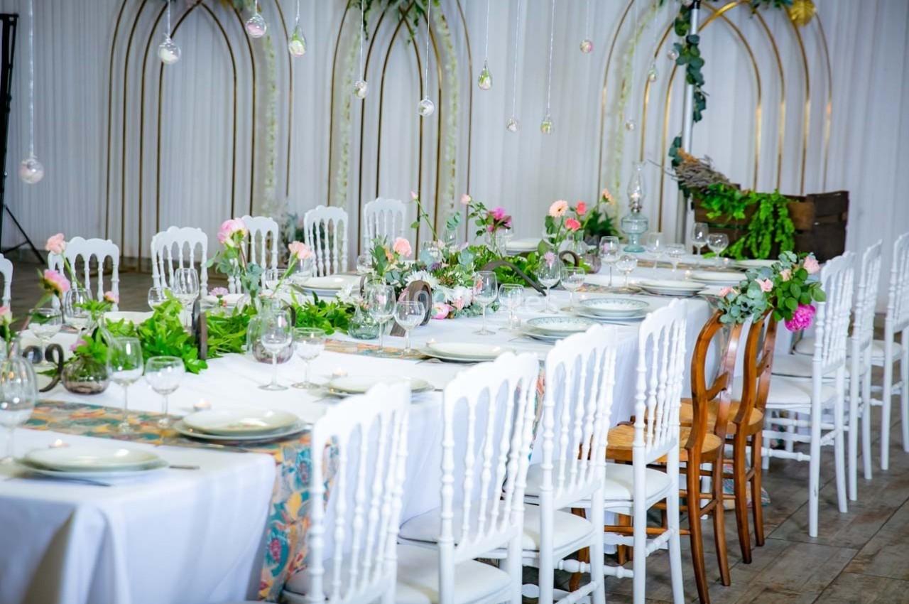 Table dressée pour un événement, ornée de nappes blanches, décorations florales et chaises blanches et en bois.