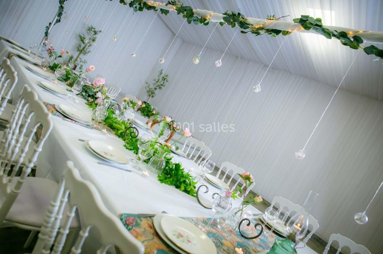 Grande table de réception décorée avec des fleurs, feuillages suspendus et vaisselle élégante dans une salle lumineuse.