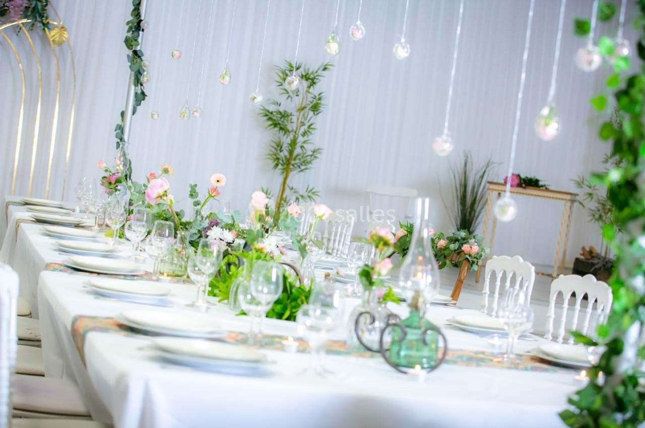Table décorée avec des fleurs, vaisselle élégante et guirlandes lumineuses suspendues dans un cadre lumineux et végétal.