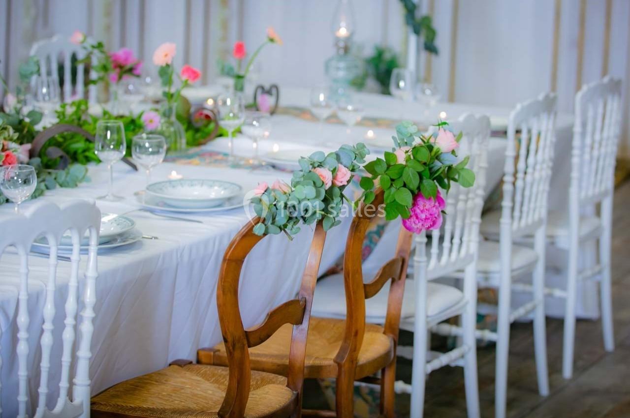 Table décorée avec des fleurs colorées, assiettes blanches et chaises en bois et en plastique dans une salle lumineuse.