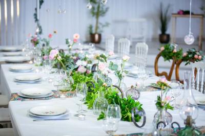 Table ronde avec verres vides, assiettes empilées, couverts, serviettes et desserts en arrière-plan.