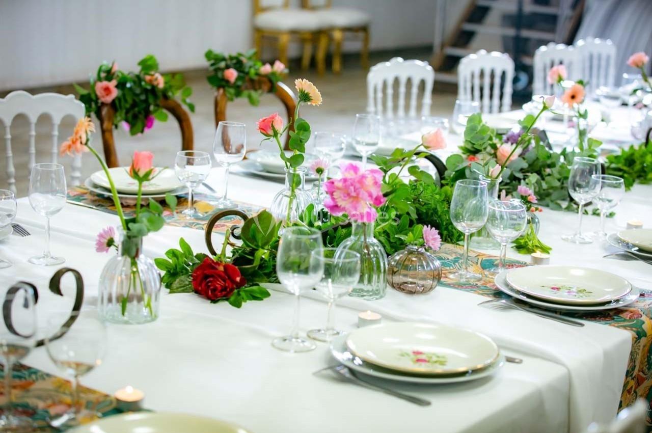 Table élégamment dressée avec nappes blanches, vaisselle, verres et décoration florale colorée.
