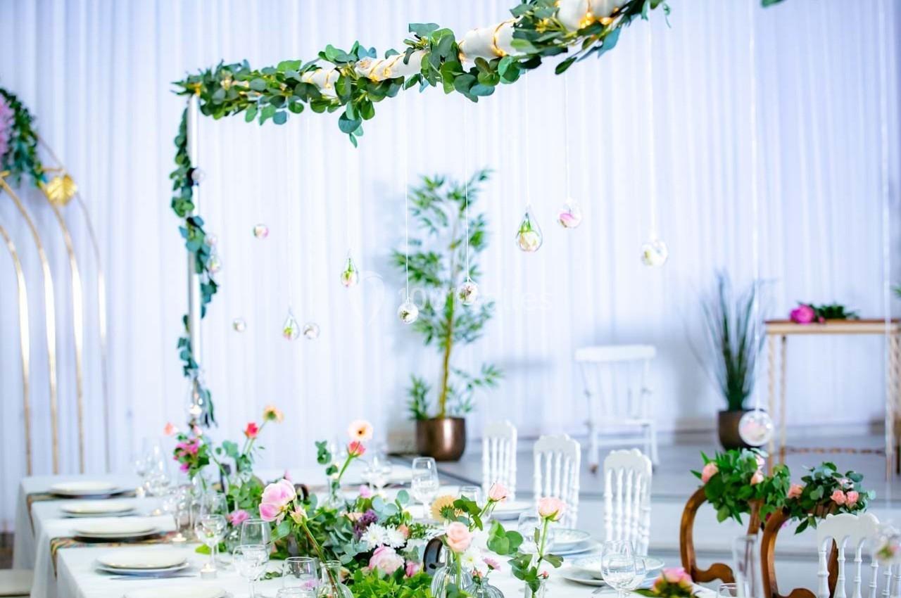 Table décorée avec des fleurs, des chaises élégantes et une guirlande suspendue dans un cadre lumineux et festif.