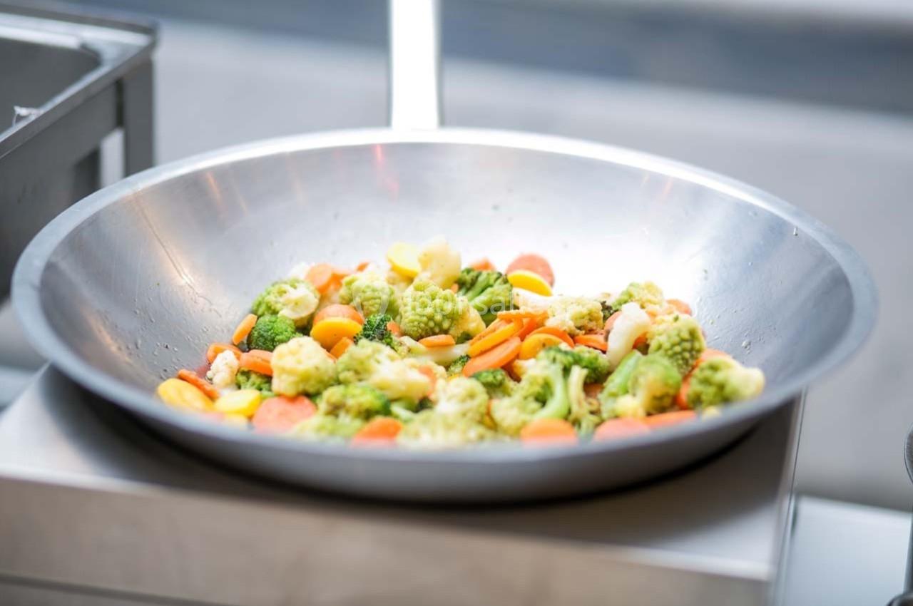 Légumes variés, dont brocolis, carottes et chou-fleur, cuits dans un grand wok en métal.