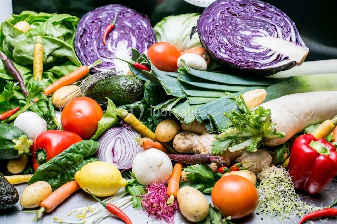 Légumes frais variés, dont choux rouges, carottes, poivrons, tomates et herbes, disposés sur une surface.