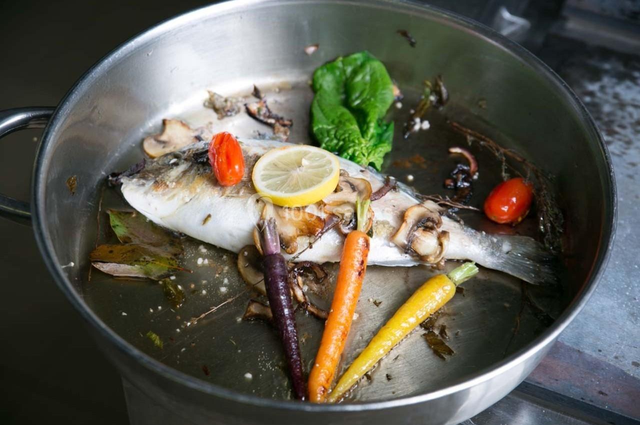 Poisson entier cuit dans une poêle avec légumes colorés, champignons, tomate cerise et tranche de citron.