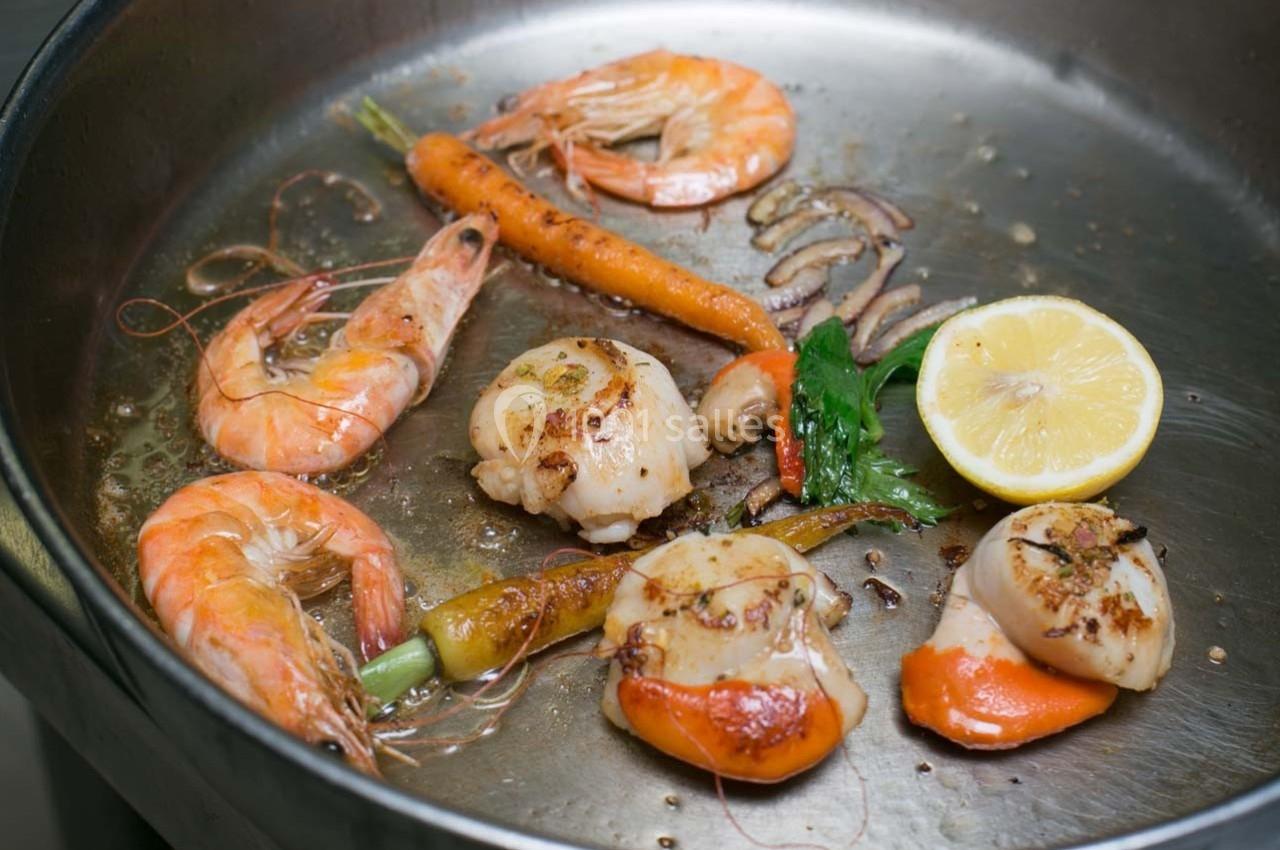 Crevettes, noix de Saint-Jacques, carottes, citron et persil cuisinés dans une poêle en métal.
