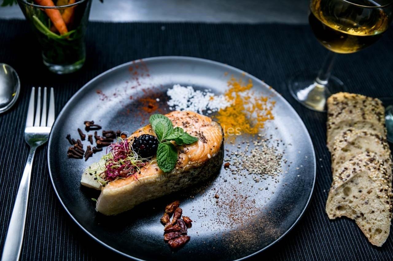 Assiette de saumon grillé garni de fines herbes, épices et baies, accompagnée de pain et d'un verre de vin blanc.