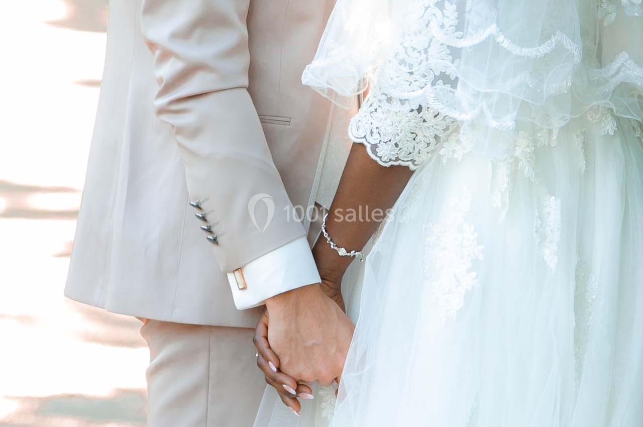 Un couple en tenue de mariage se tient la main, mettant en valeur des détails de la robe et du costume.