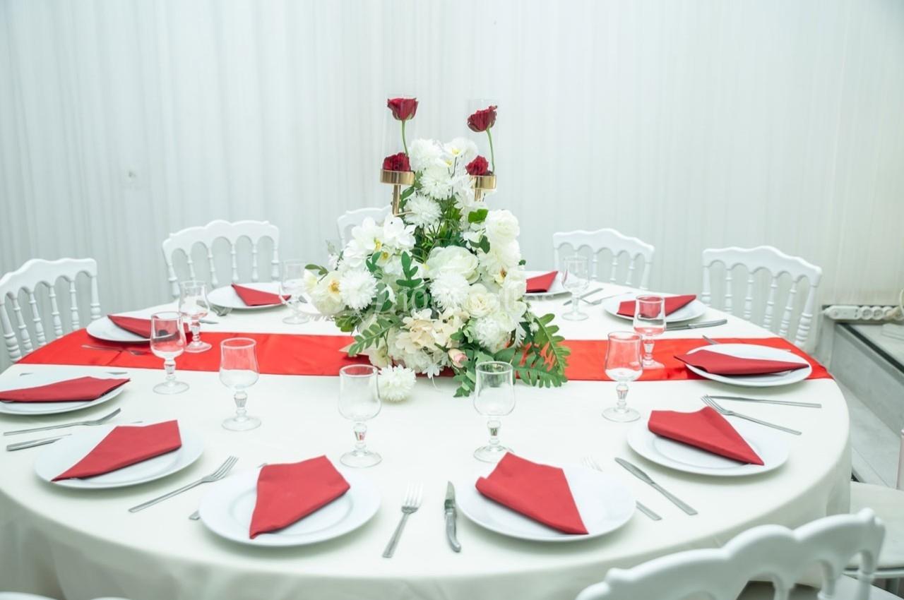 Table ronde élégamment dressée avec une nappe blanche, des serviettes rouges et un centre de table floral blanc et rouge.