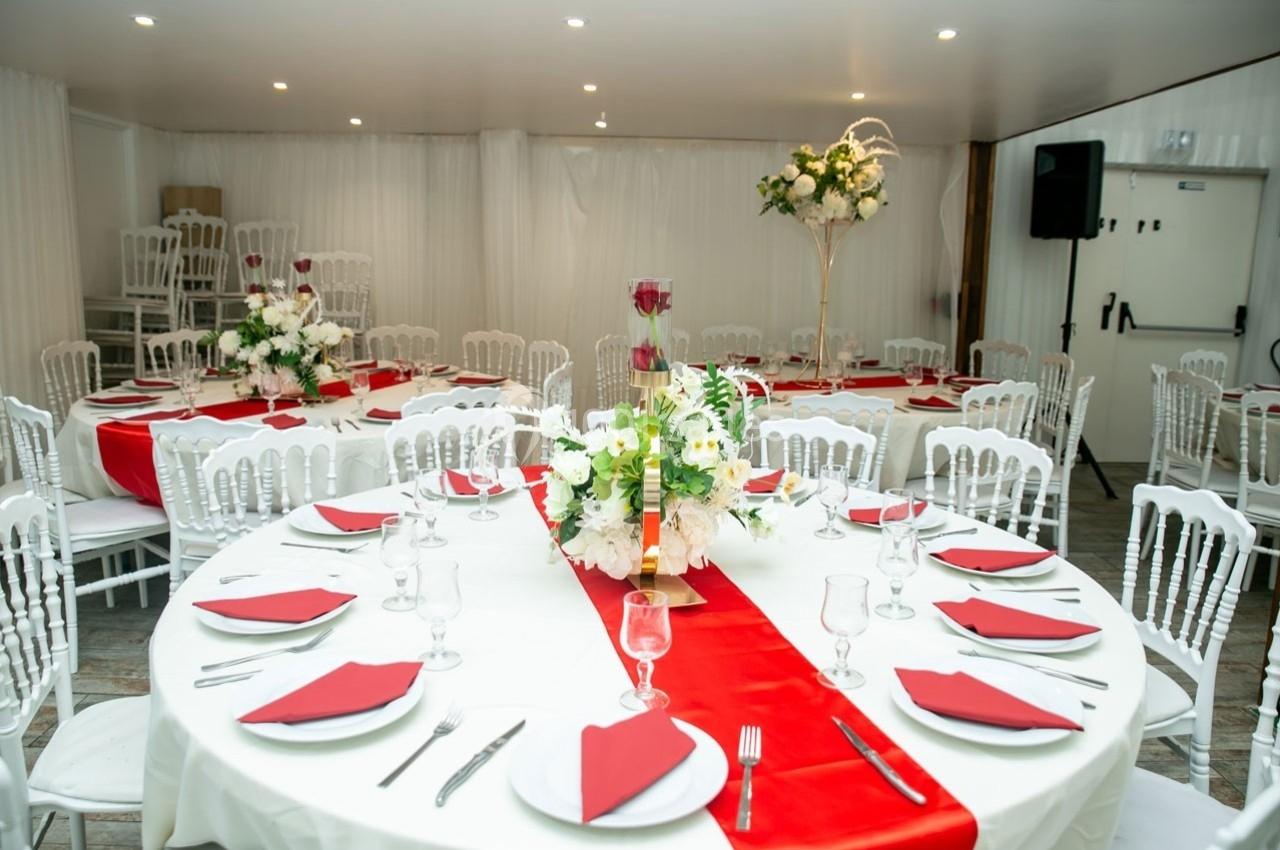 Salle de réception décorée avec des tables rondes, nappes blanches, chemins de table rouges et arrangements floraux.