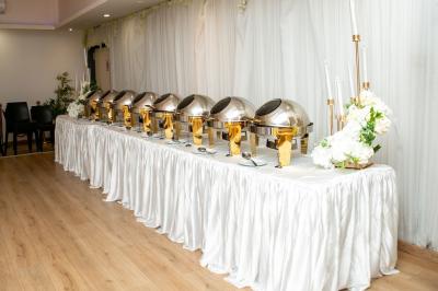 Table ronde avec verres vides, assiettes empilées, couverts, serviettes et desserts en arrière-plan.