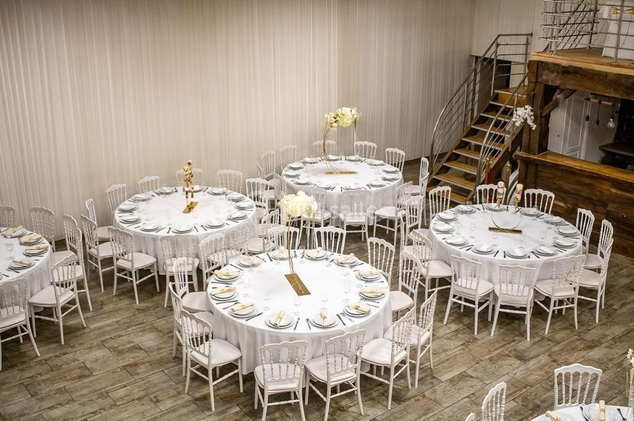 Salle de réception avec tables rondes dressées de nappes blanches, chaises assorties et décorations florales.