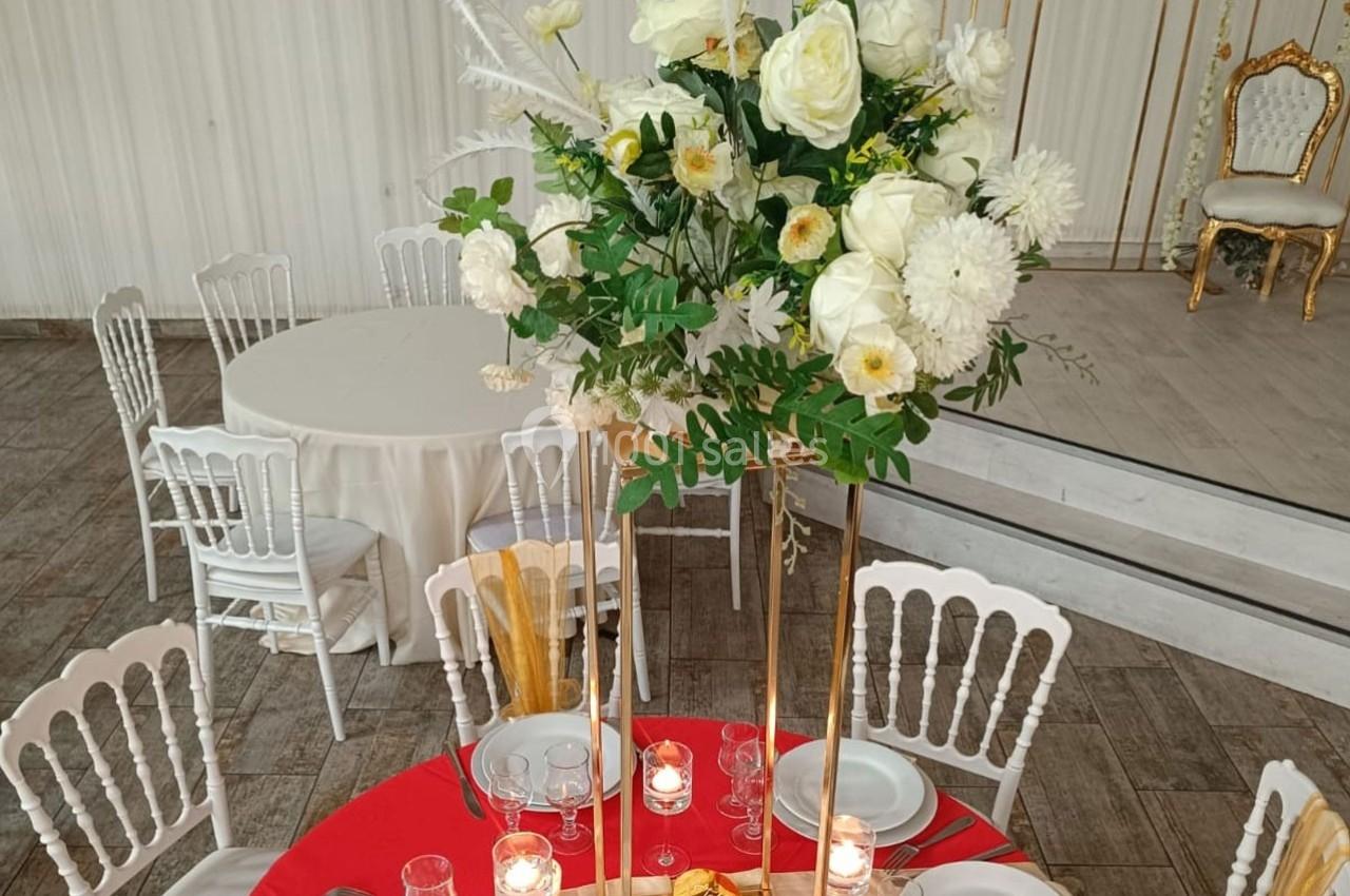 Centre de table floral avec roses blanches et verdure, entouré de bougies, sur une table dressée dans une salle de réception.
