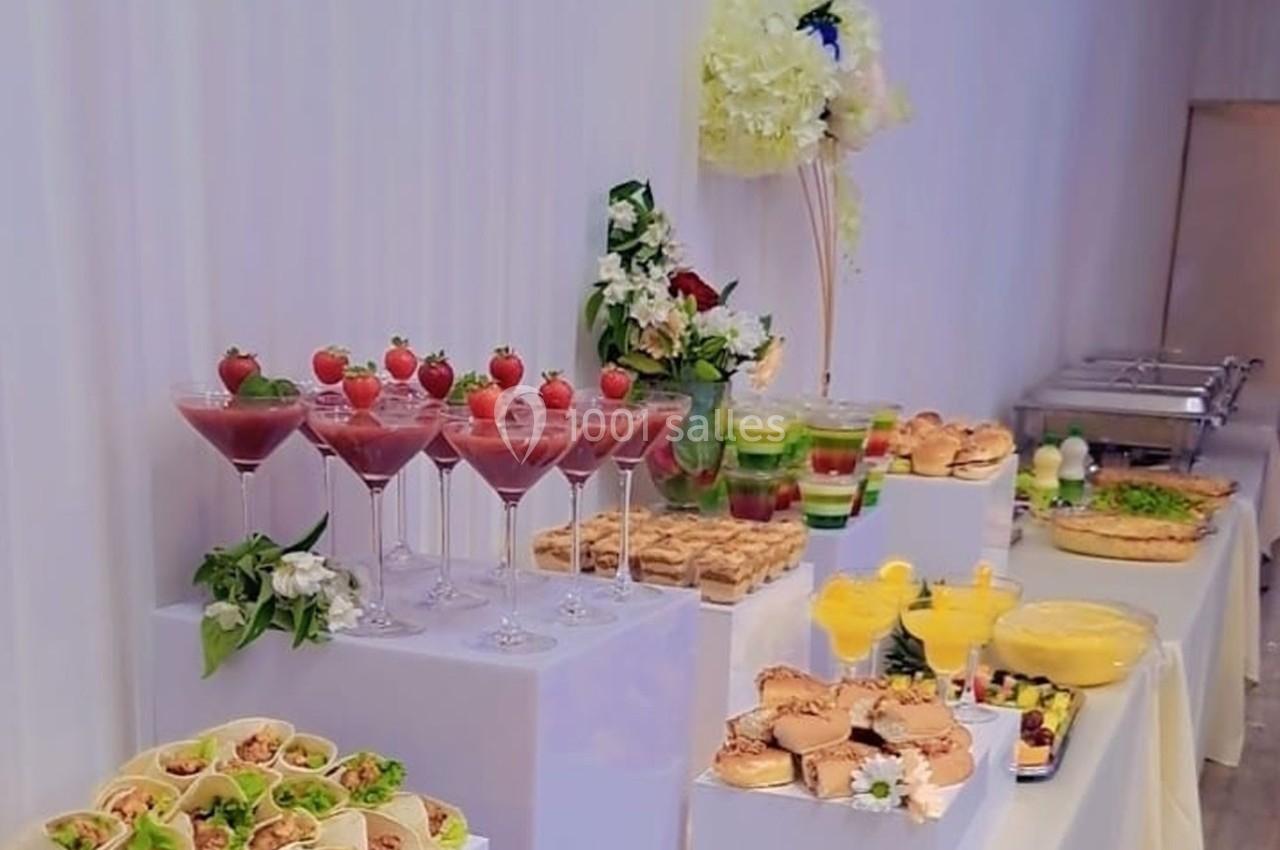 Buffet avec cocktails, verrines, plats variés et décorations florales sur des tables blanches.