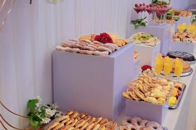 Table ronde avec verres vides, assiettes empilées, couverts, serviettes et desserts en arrière-plan.
