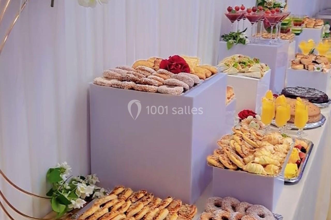 Buffet de pâtisseries variées avec viennoiseries, gâteaux, jus d'orange et décorations florales sur des présentoirs blancs.