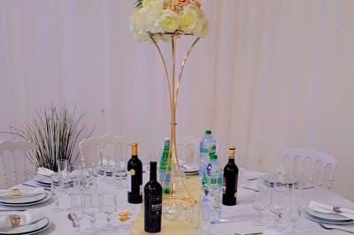 Table ronde avec verres vides, assiettes empilées, couverts, serviettes et desserts en arrière-plan.