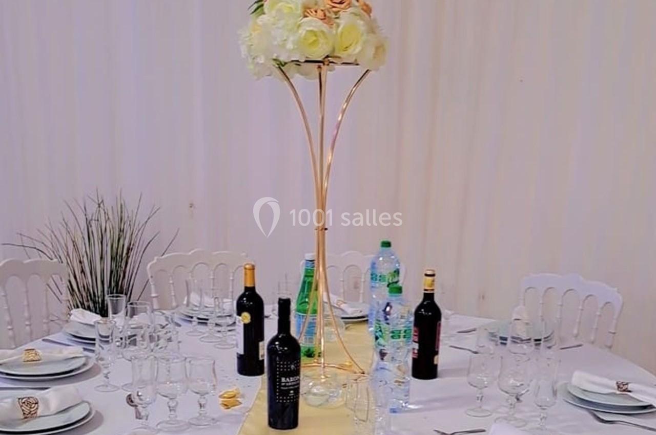 Table dressée avec nappes blanches, centre de table floral, bouteilles de vin et d'eau, et vaisselle disposée.