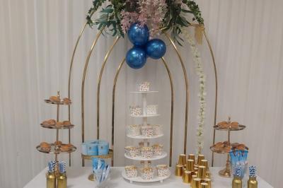 Table ronde avec verres vides, assiettes empilées, couverts, serviettes et desserts en arrière-plan.