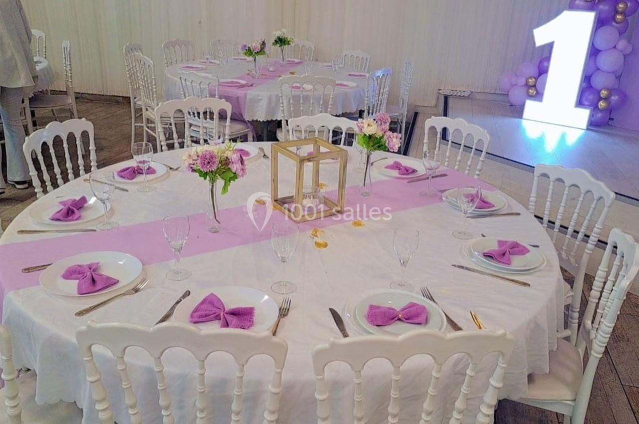 Table décorée pour un événement avec nappes blanches, chemins de table roses, serviettes pliées et centre de table floral.