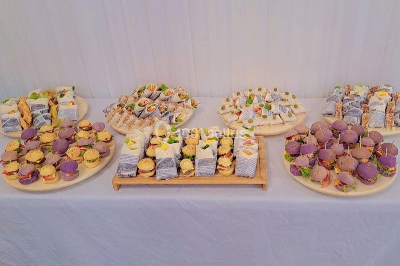 Plateaux variés de petits sandwichs et amuse-bouches colorés disposés sur une table blanche.