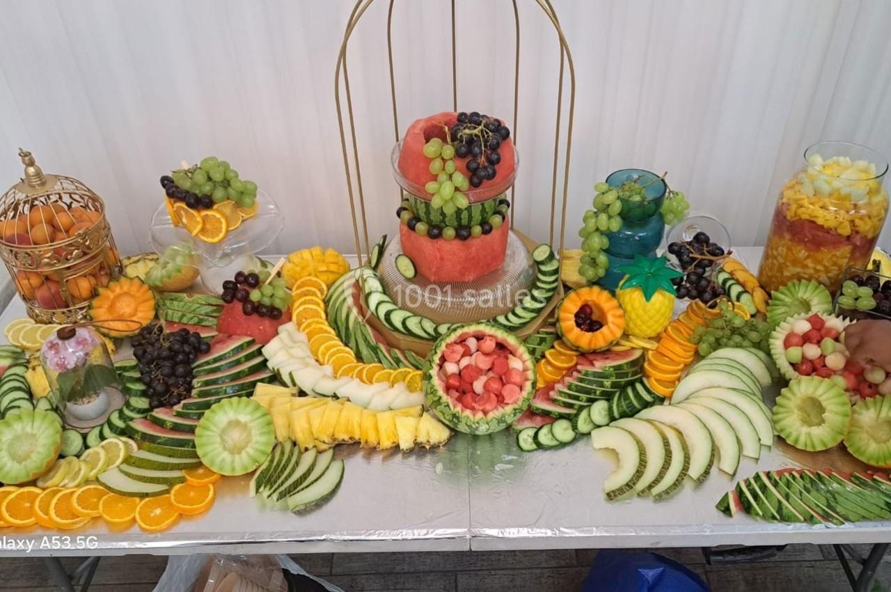 Plateau décoratif de fruits variés avec pastèque, ananas, raisins, oranges et autres fruits joliment disposés.