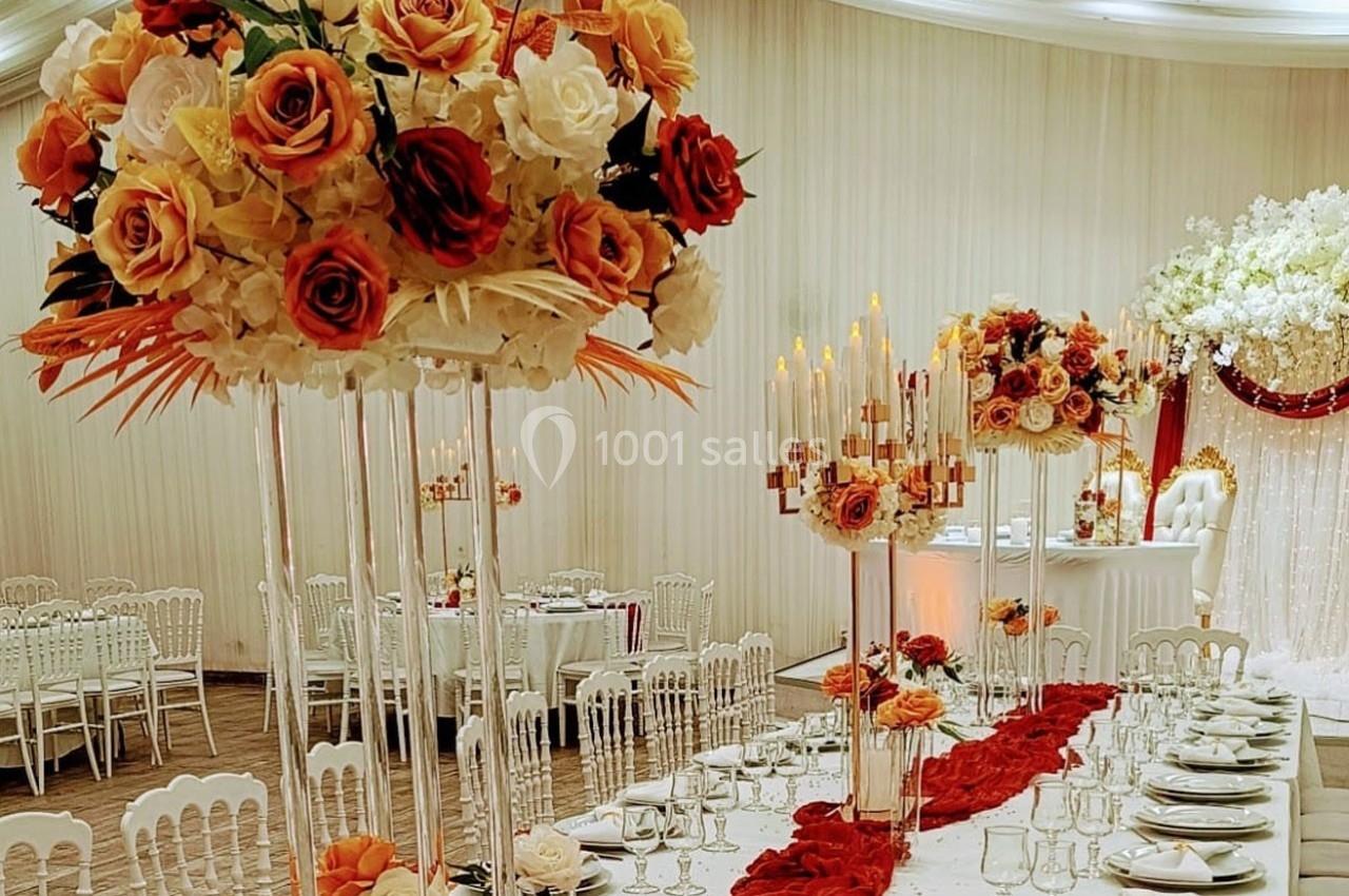 Salle de réception décorée avec des compositions florales aux tons chauds, nappes blanches et chandeliers élégants.