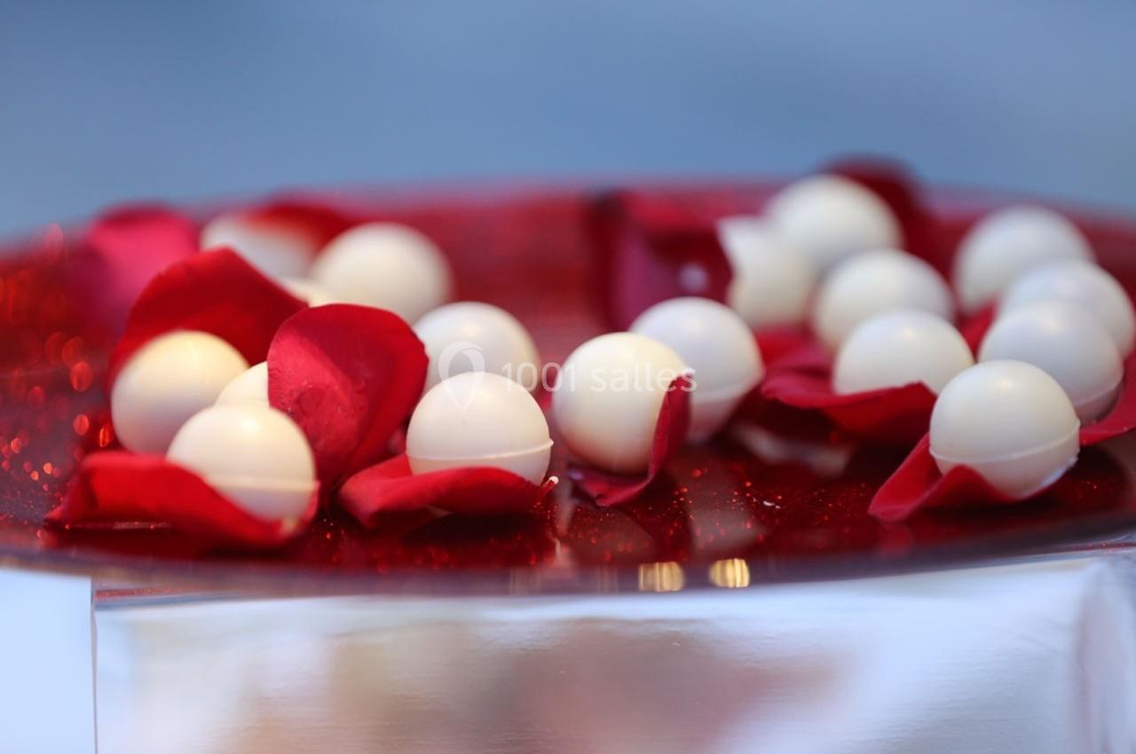 Boules blanches posées sur des pétales de rose rouges, disposées sur une surface brillante.