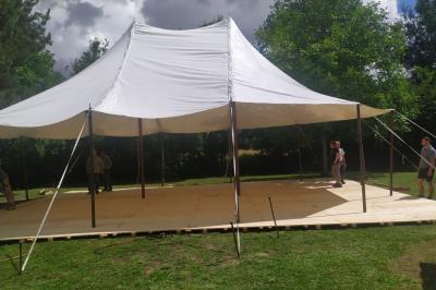 Tente blanche en cours de montage sur une structure en bois dans un espace extérieur entouré d'arbres.