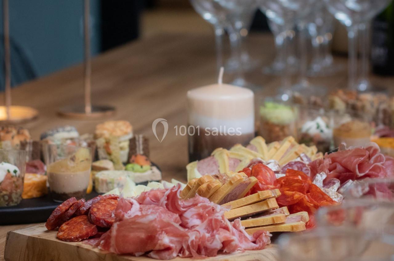 Plateau de charcuterie et fromages variés sur une table en bois, entouré de verrines et de verres à pied.