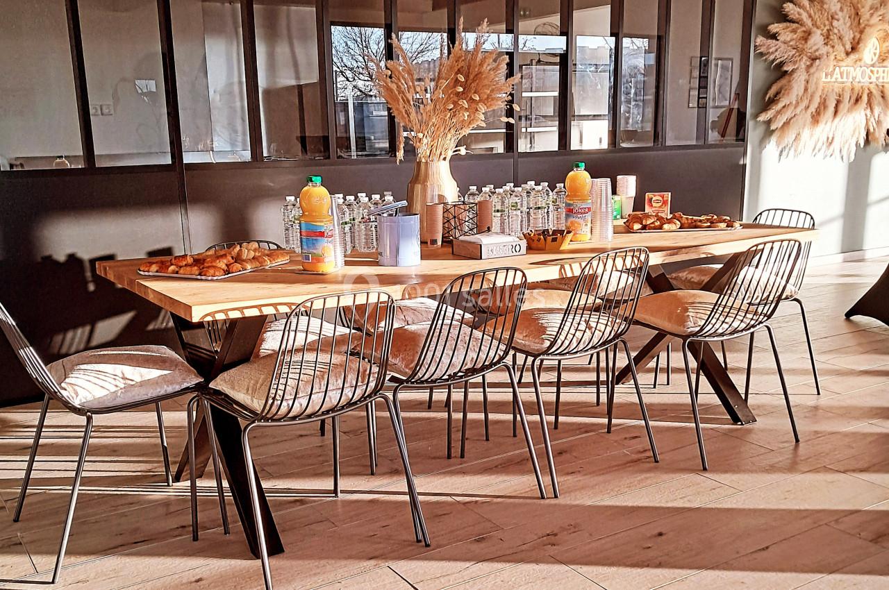 Table en bois dressée avec des boissons, viennoiseries et décorations de pampas, entourée de chaises métalliques.