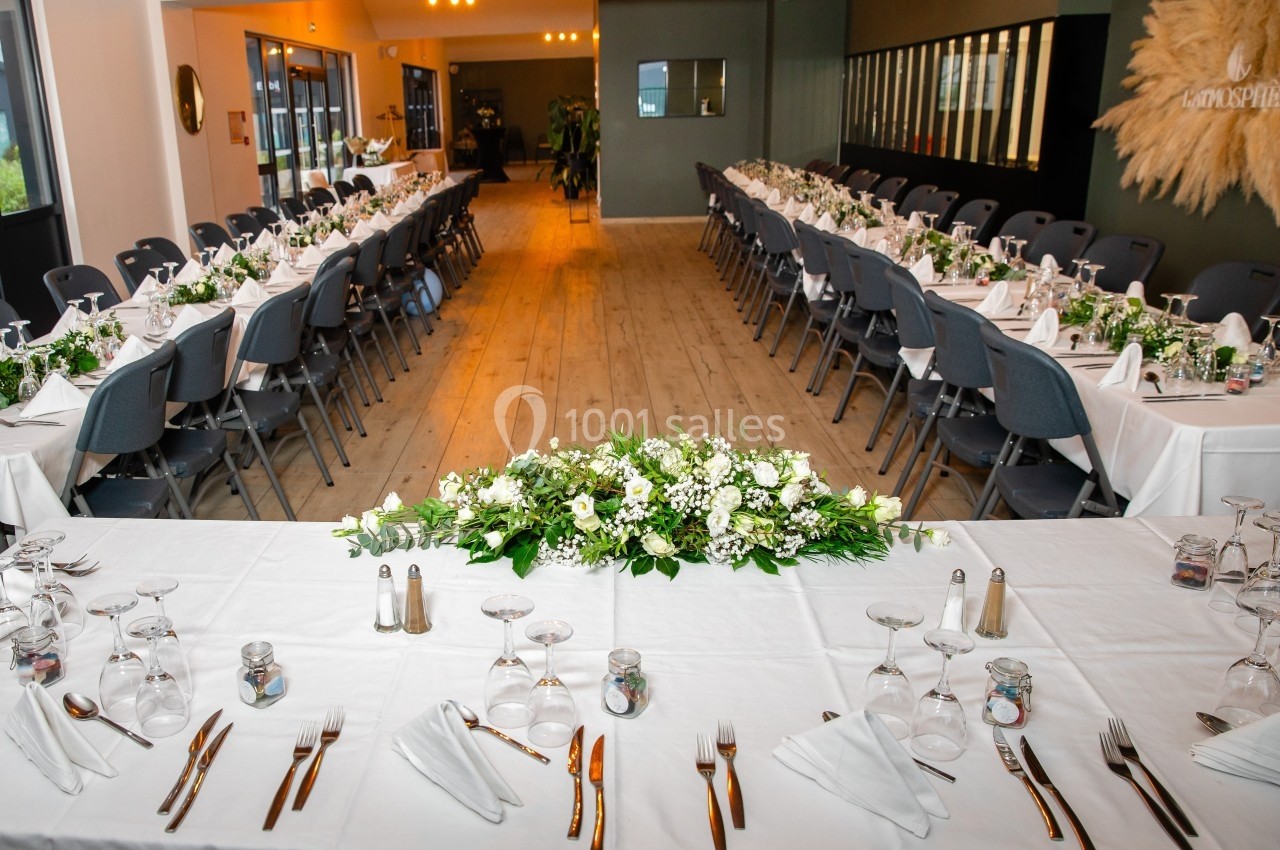 Salle de réception avec tables dressées, nappes blanches, décorations florales et couverts alignés.