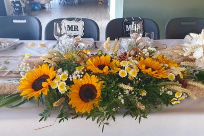 Comptoirs en bois avec décorations florales, installés en extérieur sous un ciel dégagé près de bâtiments modernes.