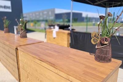 Comptoirs en bois avec décorations florales, installés en extérieur sous un ciel dégagé près de bâtiments modernes.