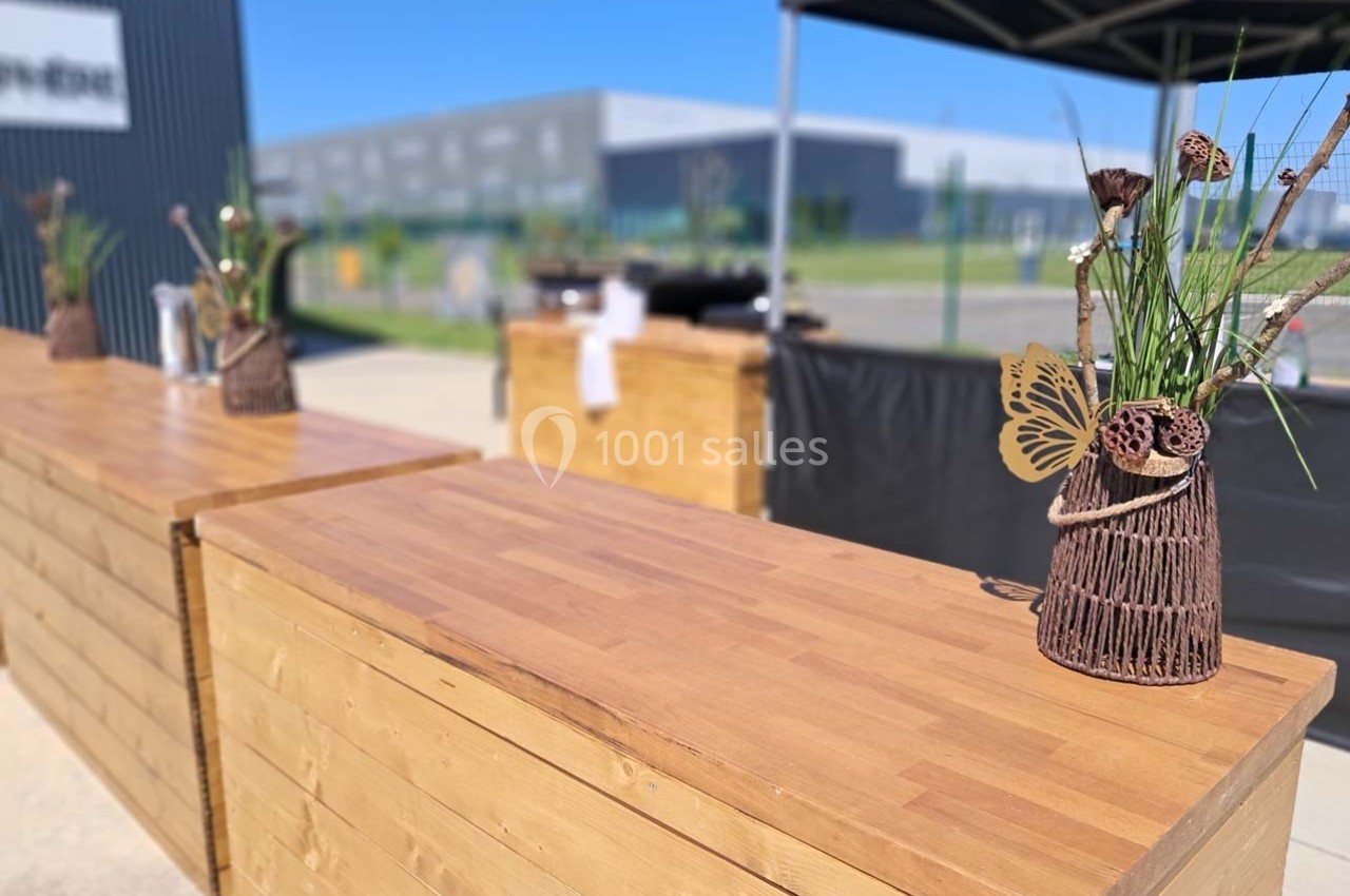 Comptoirs en bois avec décorations florales, installés en extérieur sous un ciel dégagé près de bâtiments modernes.