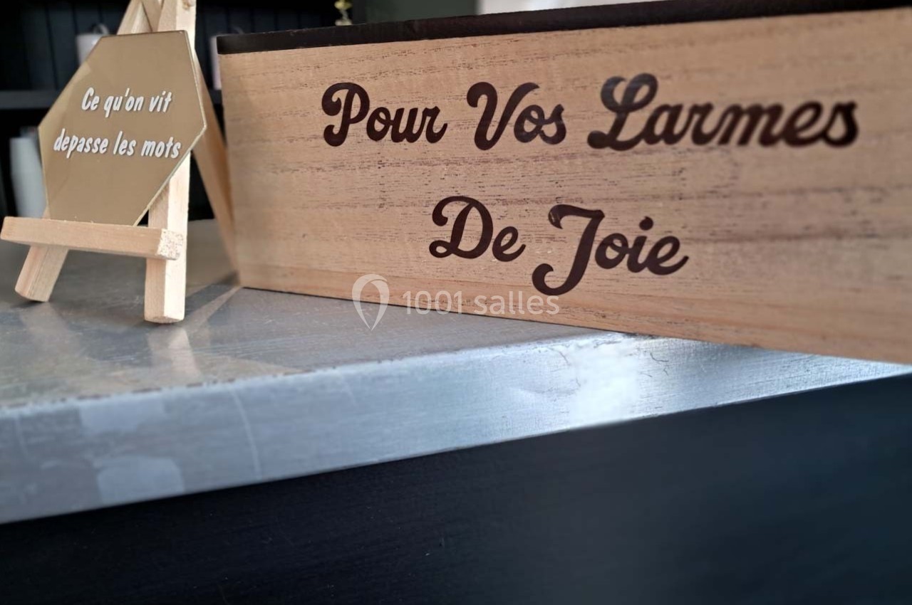 Boîte en bois avec l'inscription ’Pour Vos Larmes De Joie’ posée sur une surface près d'un chevalet décoratif.