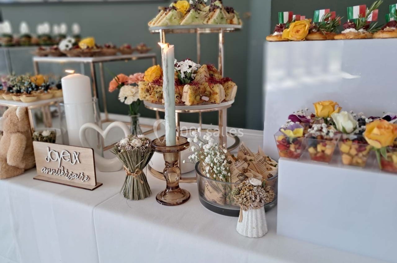 Table décorée avec des fleurs, bougies et présentoirs garnis de petits plats et desserts pour une célébration.