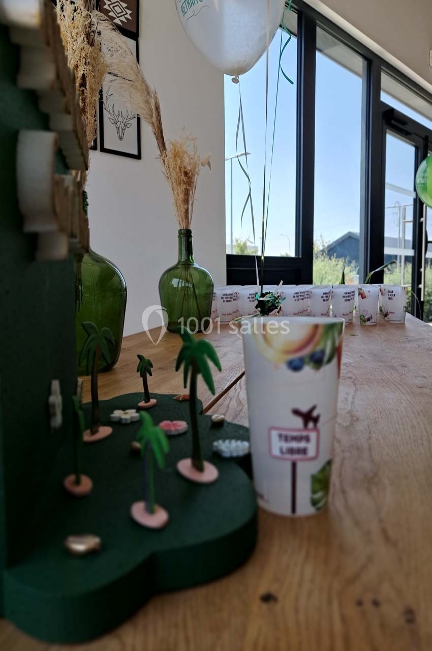 Décoration de table avec des gobelets, des ballons, des plantes miniatures et des vases près d'une fenêtre lumineuse.